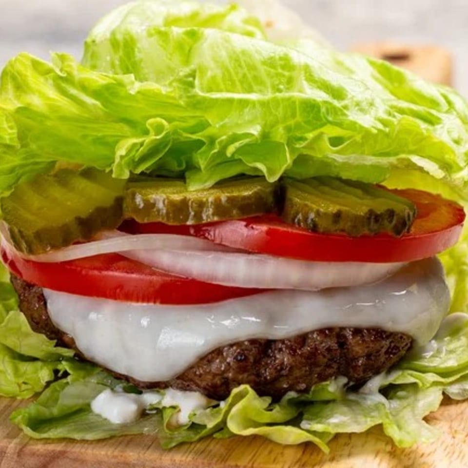 A Samz Smash burger with lettuce, pickles, tomatoes, onions, and melted cheese on a wooden board.