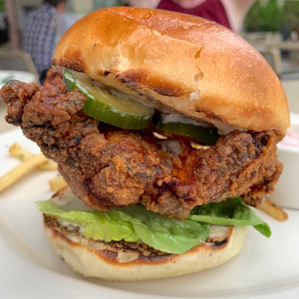 Crispy fried chicken sandwich with pickles, lettuce, and sauce on a toasted bun, with fries.