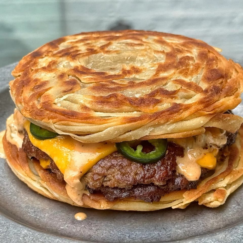Samz Smash burger with two patties, melted cheese, jalapeños, and sauce, served on a paratha bun.